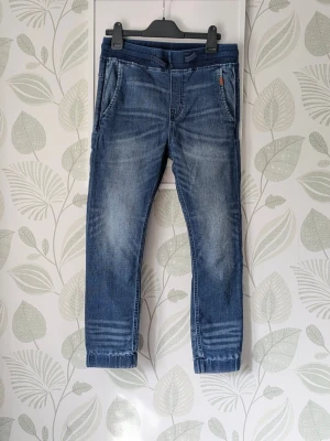 Jogger & Denmi Jeans Storlek 140 (146-152) - - Mjuka och bekväma  jeans.  - Storlek 140 men passar 146-152 bättre då den är stor i storlek.  - I fint skick. Lite ljusnad syns i mudd sam lite ludd/nopper finns i innerfickor samt syns ett litet hål i insida mudd.  - Jag kan ha missat någon miniskavank men jag har försökt att granska plagget så gott det går.