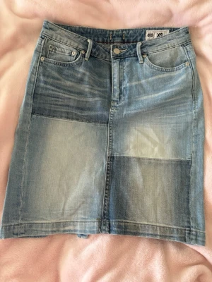 Patchwork jeanskjol från Crocker - Snygg ljusblå jeanskjol från Crocker i patchwork-stil. Kjolen har klassiska jeansdetaljer som fickor fram och bak, bälteshällor och knappstängning. Perfekt för dig som gillar en trendig och avslappnad look. Om man vill ha den kortare skulle det funka att klippa av längst ner.