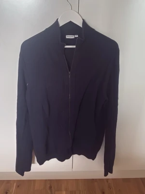 Svart ziptröja från Kappahl - Svart långärmad ziptröja från Kappahl med hög krage och ribbade detaljer. Tröjan har en stilren design med dragkedja framtill och är perfekt för lager-på-lager. Enkel att matcha med olika outfits.