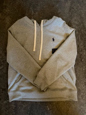 Grå hoodie från Polo Ralph Lauren - Snygg grå hoodie från Polo Ralph Lauren med klassisk logga broderad på bröstet. Riktigt skön och fin hoodie, bra passform och bra till varje dag. Använd 2-3 gånger ungefär. För fler bilder eller funderingar, skicka iväg ett meddelande.