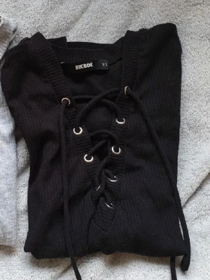 Svart långärmad topp med snörning - Svart långärmad topp från Bik Bok med snygg snörning framtill. Modellen är croppad och har en v-ringad halsringning. Perfekt för att skapa en trendig look.