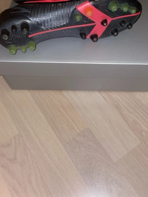Nike Mercurial svarta fotbollsskor vapor 14 - Säljer ett par Nike Mercurial fotbollsskor i svart med röda och gula detaljer. Skorna har snörning, greppvänliga dobbar och en lätt, syntetisk ovandel för bra bollkontroll. Perfekta för dig som vill ha snabbhet och stil på planen.