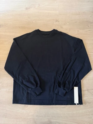 Långärmad tröja från Velour Garments - Klassisk svart långärmad tröja från Velour Garments med rund halsringning och ribbade muddar. Tillverkad i mjukt bomullsmaterial för en clean och enkel look. Perfekt att styla lager på lager eller bära som den är. Helt ny endast testad på.