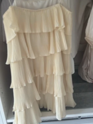 Plisserad offshoulder klänning i beige - Säljer en superfin plisserad klänning i beige med flera lager volanger. Klänningen är axelbandslös och har en flowy, romantisk look som passar perfekt till sommaren. Materialet känns lätt och luftigt, perfekt för varma dagar.