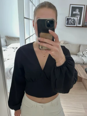 Svart topp med v-ringning - Svart topp med v-ringning och långa puffiga ärmar. Toppen är lite croppad och materialet har struktur i sig.