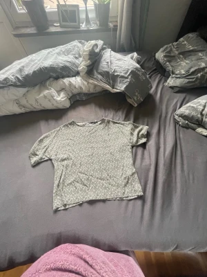 Grå mönstrad kortärmad topp - En grå topp med diskret mönster och korta ärmar. Modellen är croppad och har en avslappnad passform. Perfekt att matcha med jeans eller kjol för en trendig look.