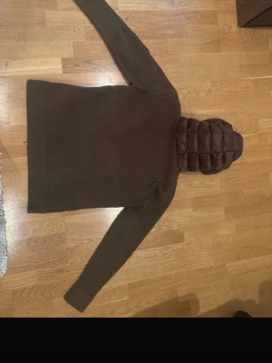 Olivgrön cardiganjacka från Moncler - Snygg olivgrön cardiganjacka från Moncler med quiltad framsida och huva. Ärmar och rygg i stickat material, medan framsidan och huvan är vadderade. Moncler-logga på ärmen. Kan sänka vid snabb affär. Storlek L  