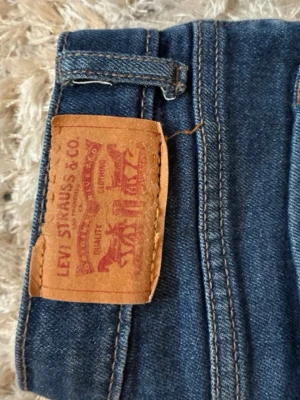 Blå Levi's jeans med klassisk passform - STORLEKEN ÄR 152/12 ÅR!!Säljer ett par blå jeans från Levi's med läderlapp bak i midjan. Det är Bootcut och läderlappen där bak sitter inte så bra och har syr några stygn i kappen med svart tråd men annars inget fel på det.