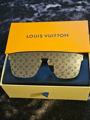 Lv svarta solglasögon - Snygga svarta solglasögon med ikoniskt LV-mönster på glaset. Sköldpaddsinspirerad båge och exklusiv design. Kommer med originalförpackning, fodral och påse. Perfekta för dig som vill ha en lyxig accessoar med statement-känsla.