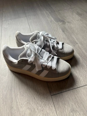 Grå Adidas sneakers med vita ränder - Snygga sneakers från Adidas i grå mocka med klassiska vita ränder på sidorna och breda vita skosnören. Skorna är endast testad annars oanvända 