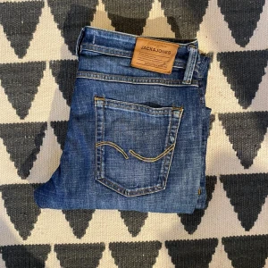 Blå jeans från Jack & Jones - Snygga blå jeans från Jack & Jones med klassisk femficksmodell och gul kontrastsöm. Jeansen har rak passform och är tillverkade i slitstarkt denimtyg. Perfekta för en avslappnad och trendig stil.