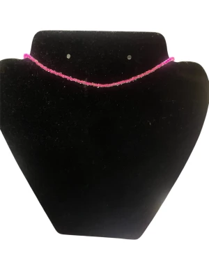 Rosa pärlhalsband i glas - Säljer ett tunt halsband med små rosa pärlor i glas. Halsbandet har en enkel och stilren design som passar perfekt till lager-på-lager eller som ett statement piece. Färgen är klarrosa och pärlorna är jämnt fördelade längs hela halsbandet.