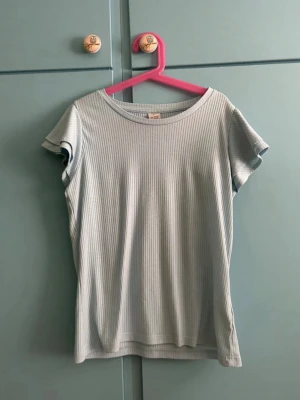 Ljusgrå ribbad t-shirt från Lindex - En stilren ljusgrå ribbad t-shirt från Lindex med korta ärmar och rund halsringning. Perfekt för en avslappnad och trendig look. Tillverkad i mjuk bomull som känns skön mot huden.💗