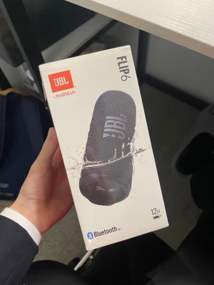 JBL Flip 6  - JBL Flip 6 är en kompakt och portabel trådlös högtalare i svart. Den har 12 timmars batteritid och är en väldigt enkelt högtalare att ha med sig överallt.