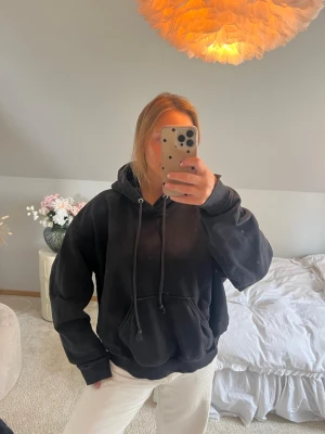 Svart oversized hoodie med huva - En svart oversized hoodie med huva och dragsnören. Hoodien har en stor magficka framtill och ribbade muddar vid ärmslut och nederkant. Perfekt för en chill och avslappnad stil.