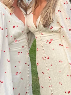 Vit adooreklänning med röda blommor - Vit adooreklänning med röda blommor. Inga defekter och perfekt för midsommar!