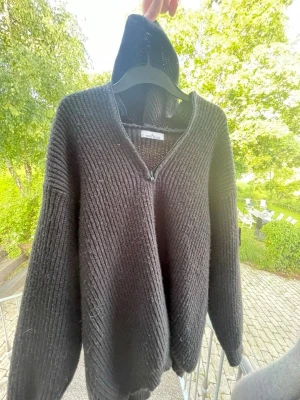Svart stickad hoodie från stone island  - Mysig svart stickad hoodie från  stone island med dragkedja framtill. Tröjan har en avslappnad passform, långa ärmar och ribbstickad struktur. Perfekt för lager på lager och chill dagar.