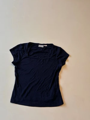 Mörkblå kortärmad topp - En enkel och stilren mörkblå topp med korta ärmar och rund halsringning. Toppen har en figurnära passform och är tillverkad i mjukt bomullsmaterial, perfekt för en clean och avslappnad look.
