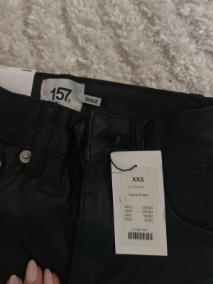 Svarta skinny jeans från 157 - Säljer ett par svarta skinny jeans från 157 med hög midja och klassisk femficksmodell. Jeansen har smal passform och dragkedja med knapp framtill. Perfekta för dig som gillar en stilren och enkel look.