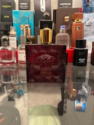 Versace Eros Flame Eau de Parfum - Versace Eros Flame Eau de Parfum i en elegant mörkröd glasflaska med guldlock. Flaskan har ett detaljerat mönster och Versaces ikoniska Medusa-huvud på framsidan. En lyxig och stilren parfym som verkligen sticker ut i badrumshyllan.