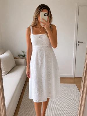 Vit broderad sommarklänning. Storlek XL. - Superfin vit klänning med broderade spetsdetaljer och breda axelband. Klänningen har en feminin, lätt utsvängd passform och är perfekt för varma dagar. Den är ärmlös och har en vacker midilängd som ger en romantisk känsla.