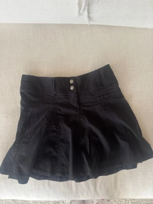 Svart lågmidjad kjol - Säljer en svart kortkjol med utsvängd passform. Vintage kjol jag fått av min mamma. Sitter väldigt snyggt på och är lågmidjad.