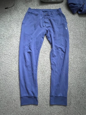 Blå mjukisbyxor från Polo Ralph Lauren - Säljer ett par blå mjukisbyxor från Polo Ralph Lauren med avslappnad passform, resår i midjan och muddar vid bensluten. Byxorna har fickor fram och en liten vit logga broderad på vänster sida. Perfekta för chill dagar hemma.