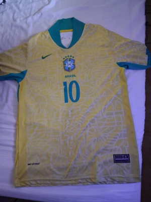 Brasilien Neymar Jr. matchtröja gul - Säljer en officiell Brasilien fotbollströja från Nike med Neymar Jr. och nummer 10 på ryggen. Tröjan är gul med gröna detaljer, har ett grafiskt mönster och Nike-logga på bröstet. Tillverkad i lätt funktionsmaterial (Nike Vaporknit) för bästa komfort.