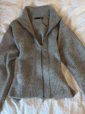 Grå ribbstickad ziptröja - Snygg grå ribbstickad tröja från Zara med dragkedja framtill och hög krage. Tröjan har en figurnära passform och långa ärmar. Perfekt för lager-på-lager och enkel att styla till olika outfits.