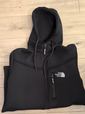 Svart hoodie från The North Face - Säljer en svart hoodie från The North Face med dragkedja framtill, justerbar huva med snören och tre fickor med dragkedja. Loggan är broderad i vitt på bröstet. Materialet känns tjockt och mjukt, perfekt för chill dagar eller när du vill ha en clean look. Helt ny oanvänd riktigt skönt nsterisln