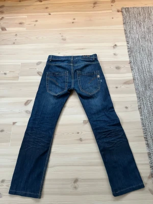 Mörkblåa jeans från dondup  - Snygga mörkblå jeans från dondup men slitningar på framsidan och insydda mönster på baksidan 