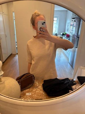 Beige stickad tröja med halvärm - Mysig beige stickad tröja med halvärm och högre rund hals. Tröjan har en enkel, rak passform och är tillverkad i ett mjukt, strukturerat material som ger en avslappnad look. Perfekt att matcha med jeans eller kjol för en stilren outfit.