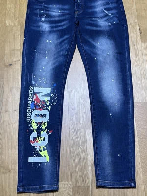  jeans - Mörkblå jeans -logga på vänster ben. Jeansen har färgstänk i gult, blått och rött samt slitningar och tvättade detaljer för en cool streetwear-look. Rak passform och klassisk femficksmodell i denim.
