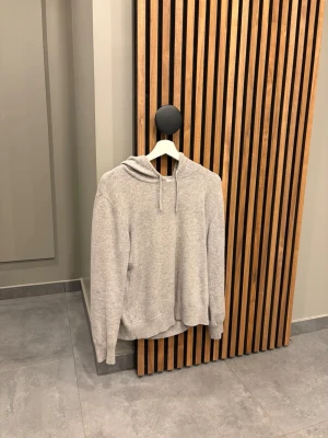 Kashmir hoodie - En stilren ljusgrå hoodie med huva och dragsnören. Hoodien har en relaxed fit och är tillverkad i kashmir, perfekt för chill dagar. Inga synliga loggor eller tryck, enkel och clean design. Långa ärmar och ribbade muddar vid ärmslut och nederkant. 