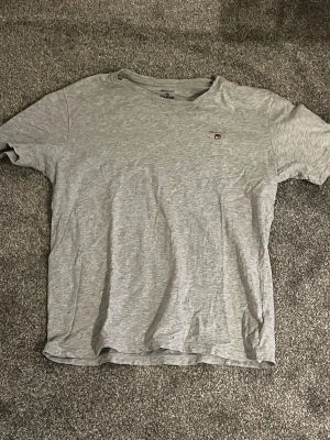 Sprillans ny Grå T-shirt från GANT i bomull - Ny Snygg grå T-shirt från GANT i mjuk bomull. Klassisk passform med korta ärmar och rund halsringning. Liten GANT-logga broderad på bröstet. Perfekt till jeans eller shorts för en clean och enkel stil. Denna t-shirt passar alla som är mellan 170 cm till 185 cm lång och vid minsta fundering eller fråga. Meddela gärna mig. Med vänliga hälsningar Eric 