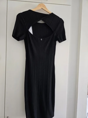 Svart klänning från Guess - Svart ribbad klänning från Guess med öppen rygg och korsade band. Klänningen har en liten metall-logga baktill och är figurnära i modellen. Oanvänd, sitter för tajt på mig. 