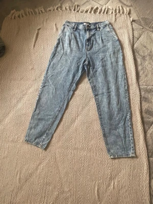 Ljusa mom jeans med hög midja - Säljer ett par ljusblå mom jeans med hög midja och avsmalnande ben. Klassisk femficksmodell med bälteshällor och dragkedja. Perfekta för en avslappnad och trendig look.