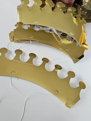 Guldiga papperskronor till maskerad - Säljer 18 guldiga kronor i papper, perfekta till maskerad eller temafest. Kronorna har en klassisk form med rundade toppar och elastiskt band för att sitta på plats. Insidan är vit och utsidan glänsande guldfärgad.