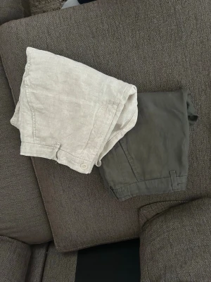 Linnebyxor från Zara - Säljer ett par beiga och khaki gröna linnebyxor med avslappnad passform och resår i midjan. Byxorna har raka ben och bakfickor, perfekta för en chill och luftig stil. Materialet är 100% linne vilket gör dem svala och sköna under varma dagar. 200kr för bägge eller 150kr styck