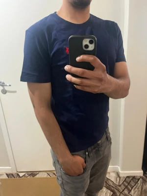 Mörkblå t-shirt från Polo Ralph Lauren - Snygg mörkblå t-shirt från Polo Ralph Lauren med klassisk röd logga broderad på bröstet. T-shirten har rund halsringning och korta ärmar. Tillverkad i mjuk bomull för en bekväm känsla och passar perfekt till jeans eller shorts.