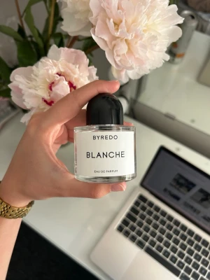 Byredo Blanche Eau de Parfum - Byredo Blanche Eau de Parfum i en stilren, rund glasflaska med svart kupolformad kork. Flaskan har en minimalistisk vit etikett med svart text. Doften är känd för sin fräscha och rena karaktär, perfekt för dig som gillar subtila och eleganta parfymer.