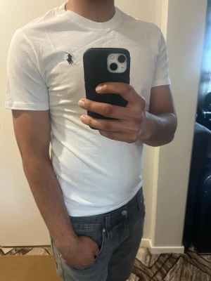 Vit t-shirt från Polo Ralph Lauren - Klassisk vit t-shirt från Polo Ralph Lauren med den ikoniska broderade loggan på bröstet. T-shirten har rund hals, korta ärmar och är tillverkad i mjuk bomull för en bekväm passform. Perfekt basplagg med stilren design.