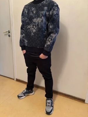 sweatshirt  - Cool sweatshirt  i mörkblått med grått och vitt blommönster. Tröjan har rund hals, ribbade muddar och en relaxed fit. Perfekt för dig som vill ha en unik och trendig look.