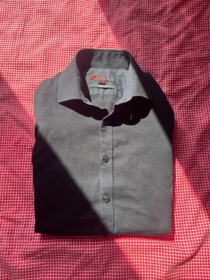 Svart slim fit skjorta S - Snygg svart skjorta i slim fit från Dressman med diskret mönstrat innerfoder i kragen. Skjortan har klassisk krage och knäppning framtill. Perfekt för dig som gillar en stilren look.