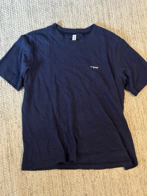 Mörkblå t-shirt med tryck original - En enkel mörkblå t-shirt med liten vit text 'original' på bröstet. Klassisk rund halsringning och korta ärmar. Perfekt basplagg som passar till allt.