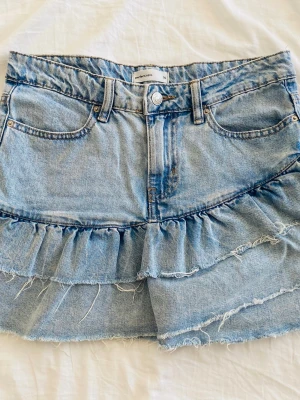 Blå jeanskjol med volang  - Supersnygg ljusblå jeanskjol från Gina tricot med volangdetalj och råa kanter. Klassisk femficksmodell med knapp och dragkedja framtill. Gjord i denim med en cool, avslappnad vibe och trendig fransig finish. Perfekt för dig som gillar en unik twist på jeanslooken. Skriv för fler bilder🥰