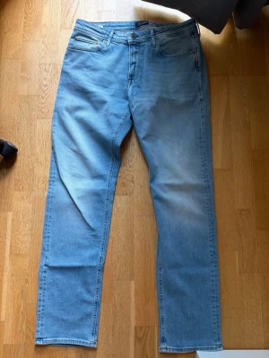 Jack & Jones Clark Regular Fit Jeans (33W/34L) - Säljer ett par ljusblå jeans från Jack & Jones med klassisk femficksmodell och raka ben. Jeansen har en snygg tvättad look och är tillverkade i mjukt denimtyg. Perfekta för en avslappnad stil och passar till det mesta. Skick: Helt nya, använda en gång under 30 min. Köpta från Jack & Jones butiken för 900 kr! 33W och 34L
