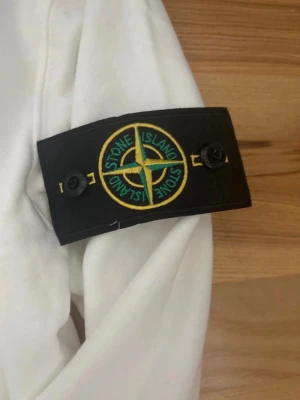 Vit sweatshirt från Stone Island - Säljer en clean vit sweatshirt från Stone Island med den ikoniska kompassen på ärmen. Tröjan har rund hals, långa ärmar och ribbade muddar. Perfekt för dig som gillar streetwear och vill ha en stilren look. Tröjan är helt ny och säljer den pågrun av att den var för liten. 