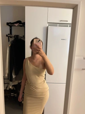 Beige oneshoulder  - Snygg beige långklänning med oneshoulder-design och figurnära passform. Klänningen har en enkel och stilren look, den är väldigt fin och elegant. Den har ett litet håll men knappt något som syns