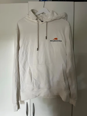 Vit hoodie från Zara - Säljer en stilren vit hoodie med liten logga och orange detalj på bröstet. Hoodien har huva med dragsko och en stor magficka framtill. Tillverkad i mjukt material och har långa ärmar. Perfekt för dig som gillar exklusiva streetwear-plagg.